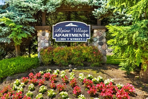 a sign for alpine village apartments in front of a garden