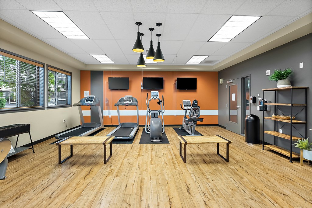 a fitness center with treadmills and benches in a room with a wood floor