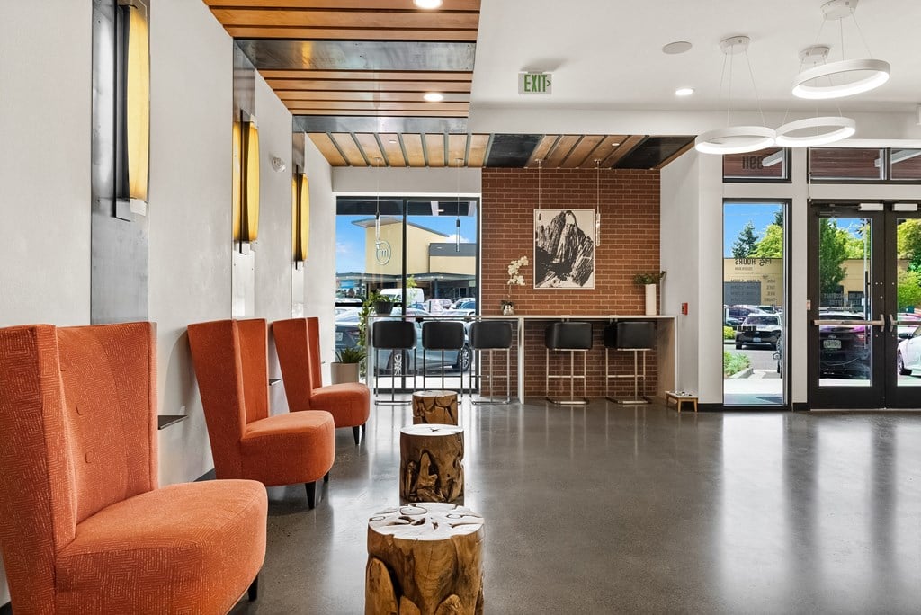the lobby of a hotel with orange chairs and a bar and a glass door
