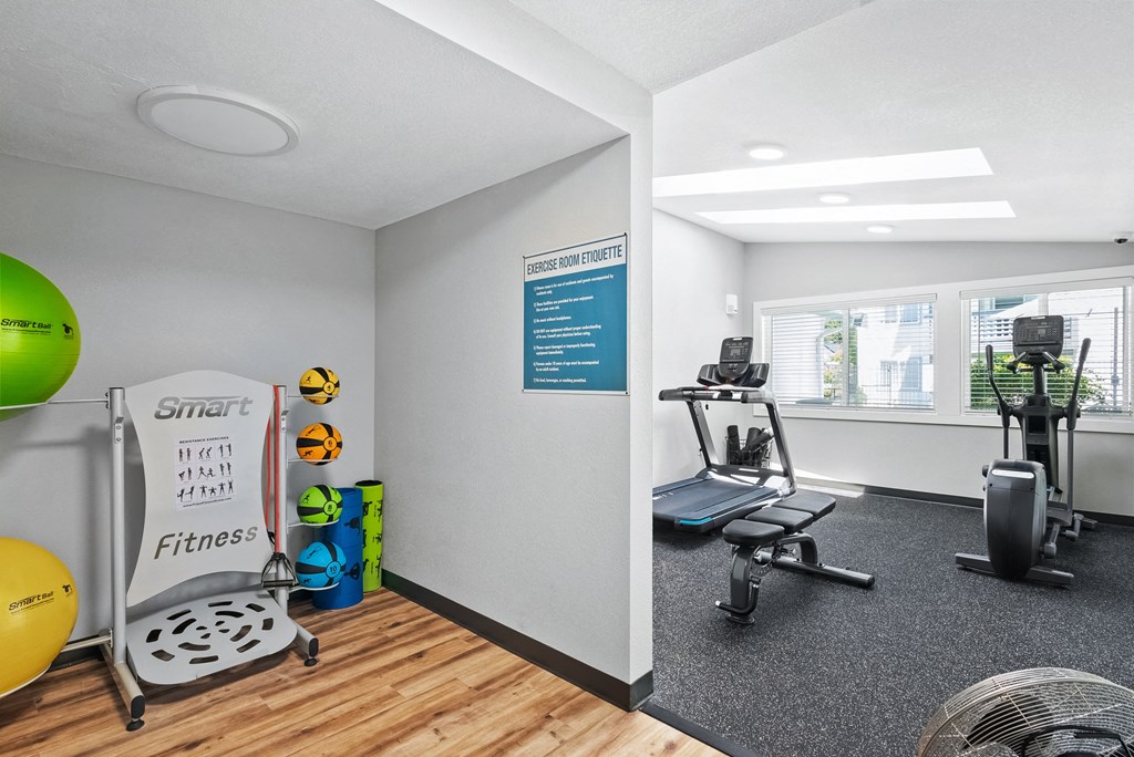 a gym with a treadmill and weights on the floor and a window