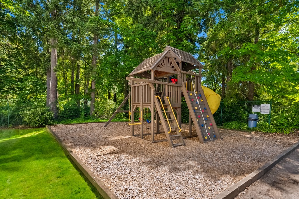 a swing set in a backyard with trees and a yellow slide