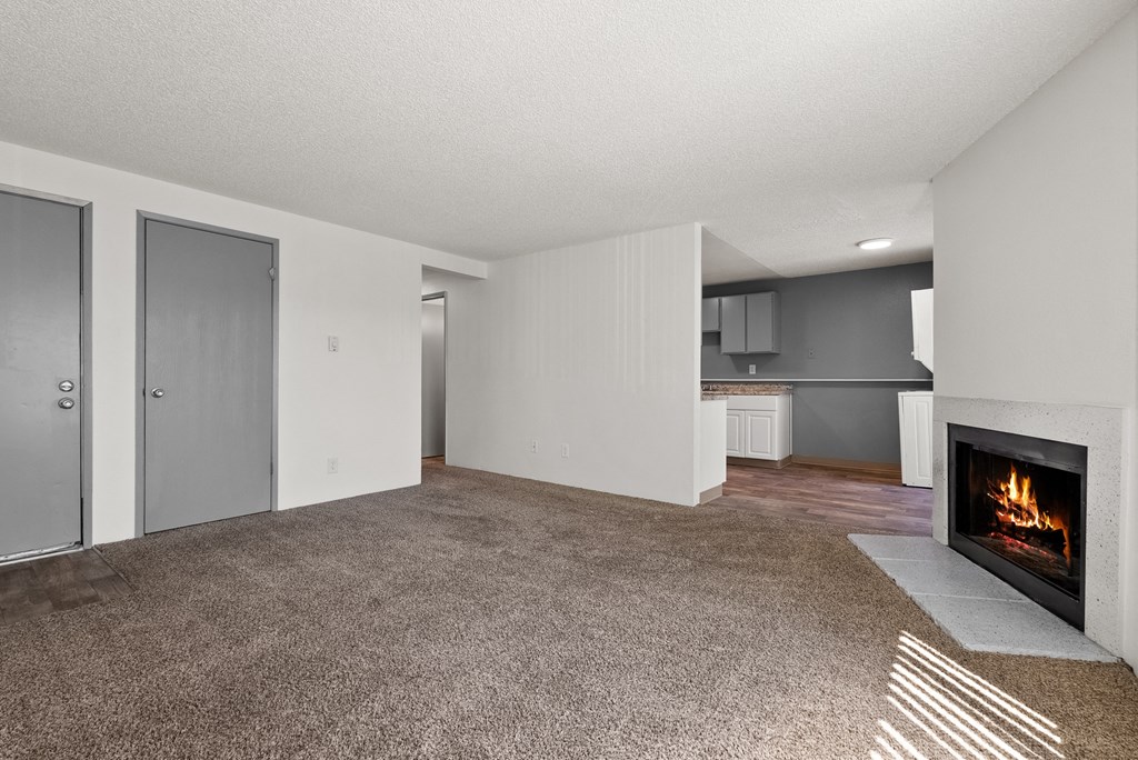 an empty living room with a fireplace and a kitchen
