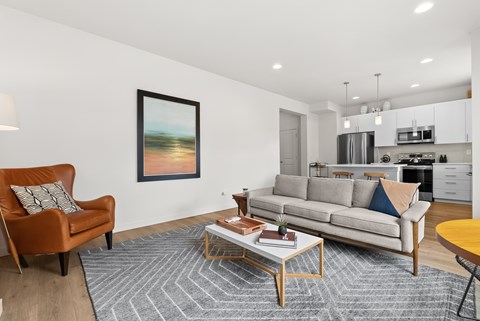 A living room with a brown chair, a grey couch, a coffee table, and a painting on the wall.