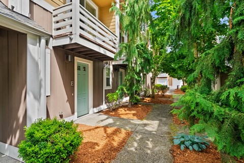 a walkway between two buildings with trees and a green door