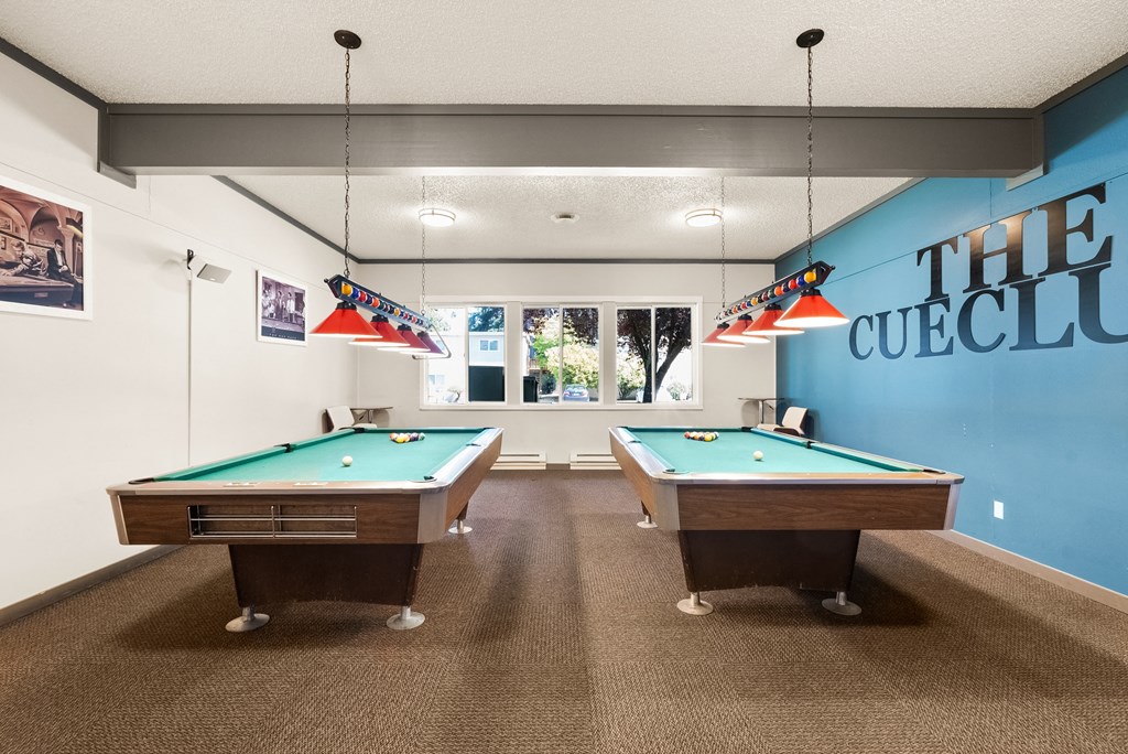two pool tables in a room with a blue wall with a window and a pool