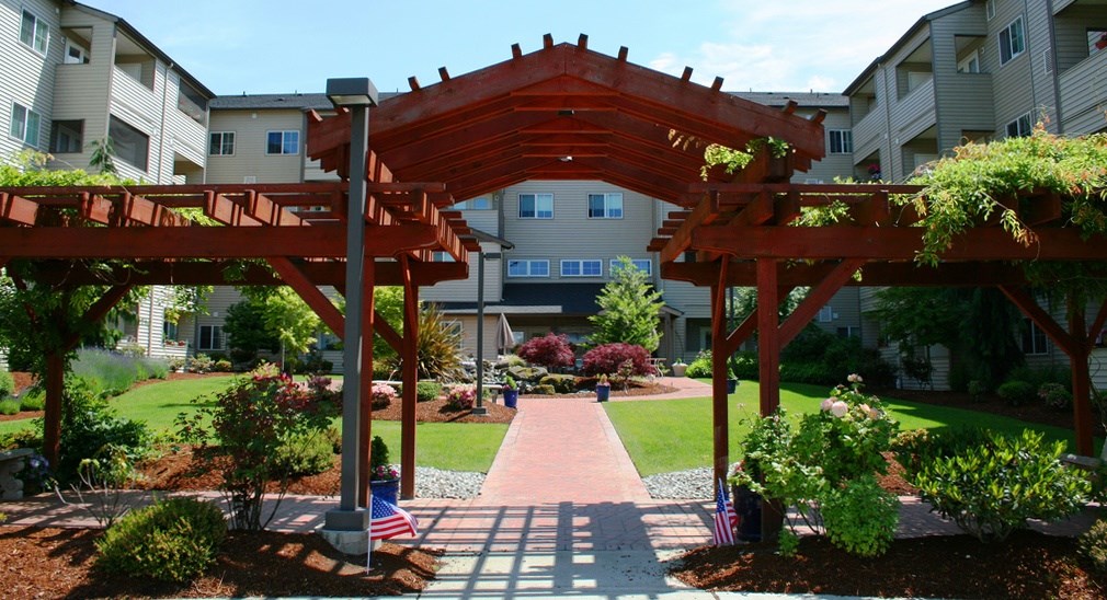 a wooden gazebo in a garden with apartments in the background