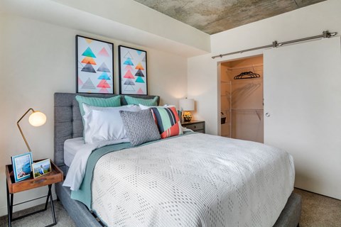 A bedroom with a bed, pillows, a nightstand, and a wall-mounted light fixture.