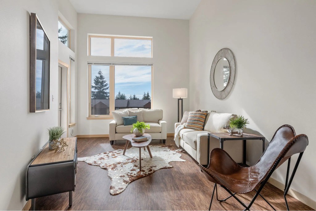 A living room with a white couch, a brown leather chair, and a rug with a cowhide pattern.