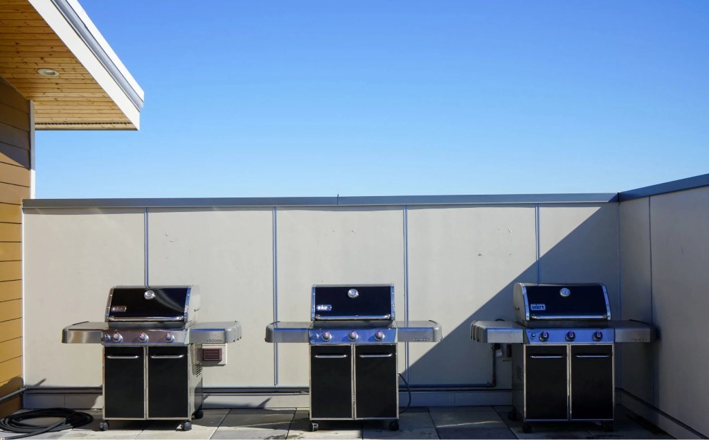 Three barbecue grills are lined up on a patio.
