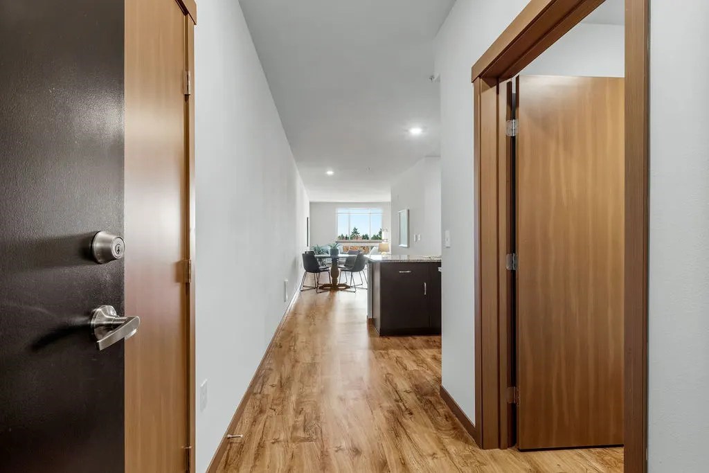A long hallway with a black door on the left and a wooden door on the right.