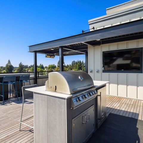 A BBQ grill is on a deck with a table and chairs.