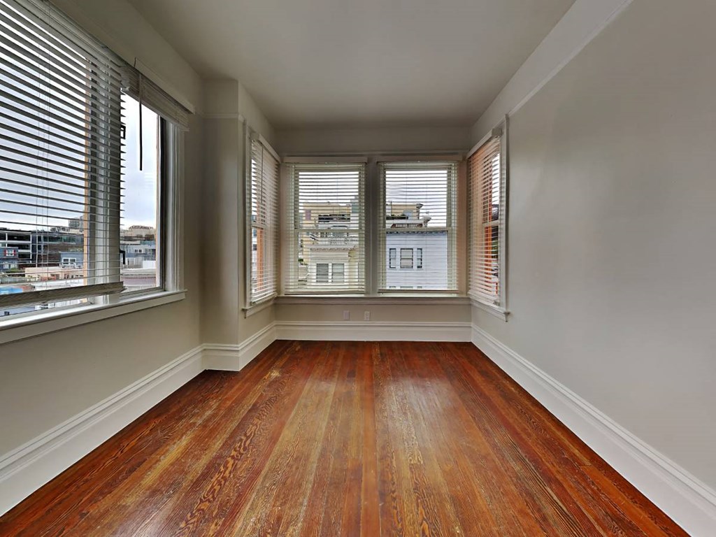 an empty living room with three windows and wood floors