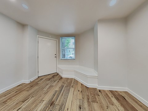 a living room with white walls and wood flooring and a window