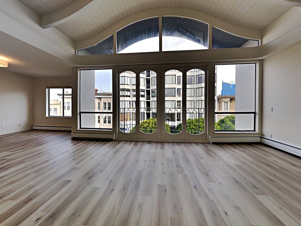 an empty living room with large windows and wooden floors