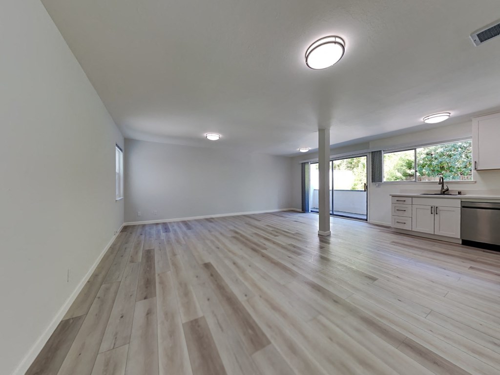 an empty living room and kitchen with wood floors and white walls