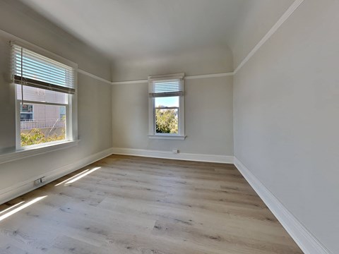 an empty room with two windows and wood flooring