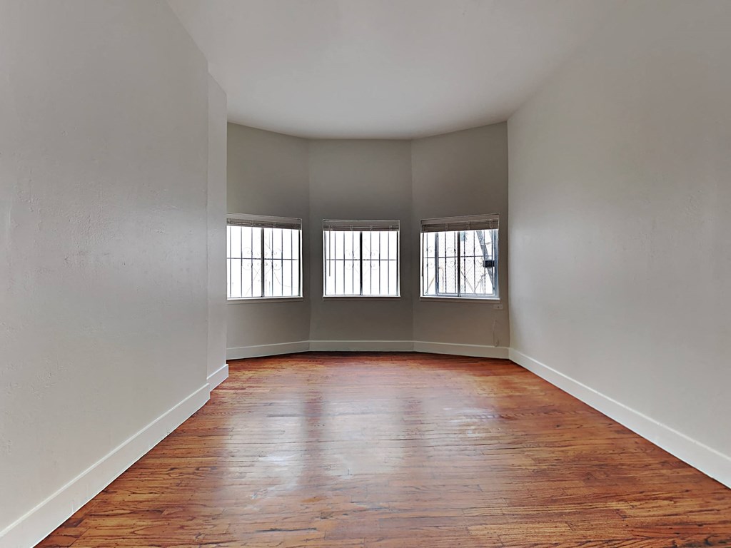 an empty living room with wood floors and three windows