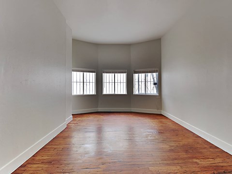 an empty living room with wood floors and three windows