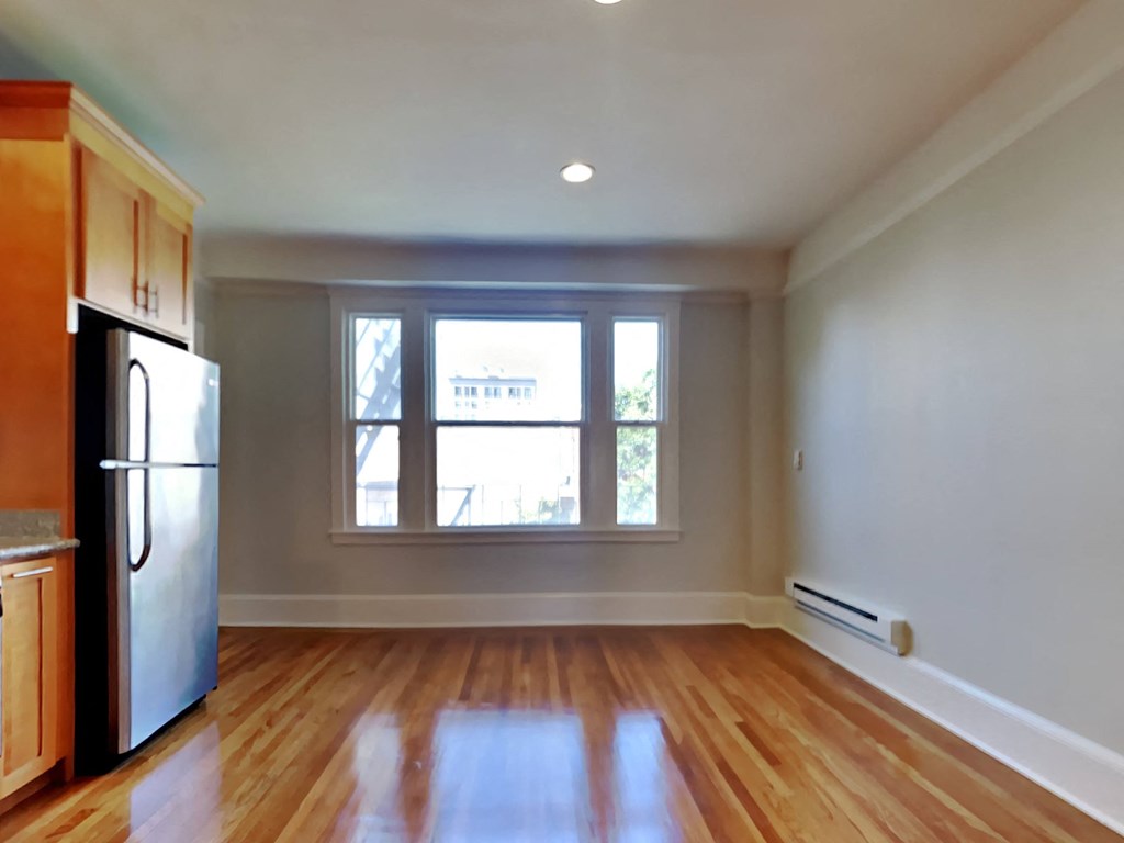 an empty living room with a refrigerator and a window