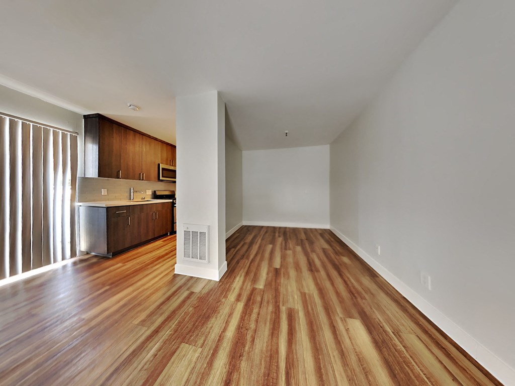 an empty living room with wood flooring and a kitchen
