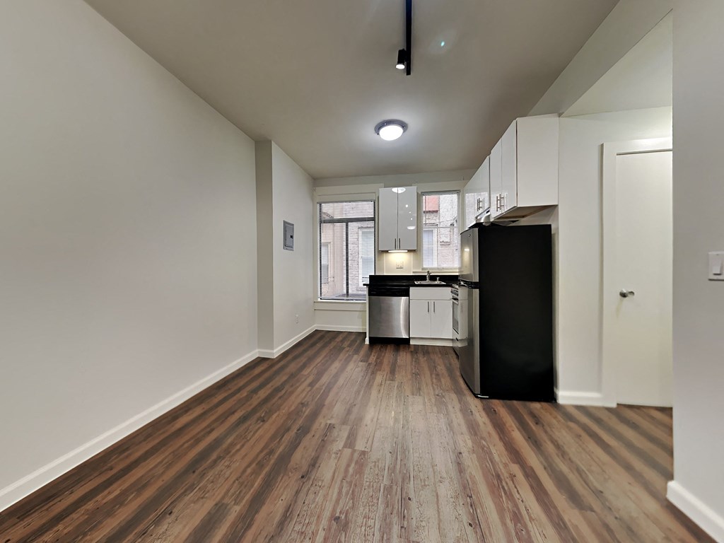 an empty living room and kitchen with wood floors and white walls
