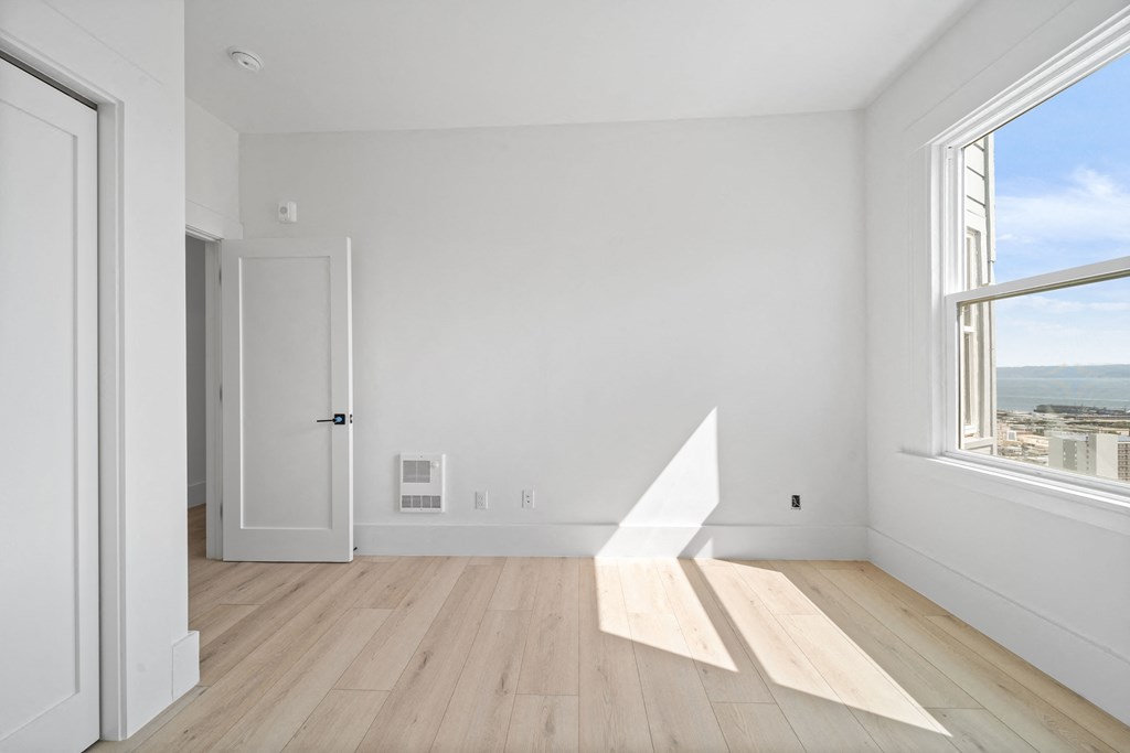 a living room with white walls and wooden floors and a large window