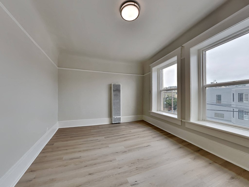 an empty living room with two large windows and wood flooring