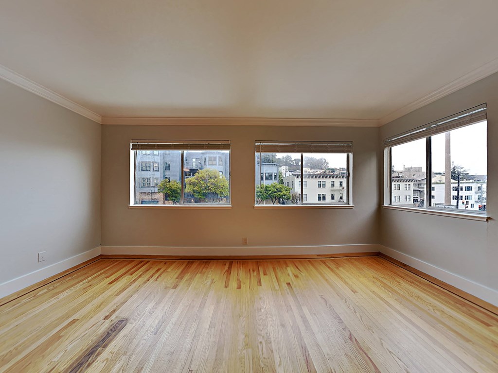 an empty living room with wood floors and three windows