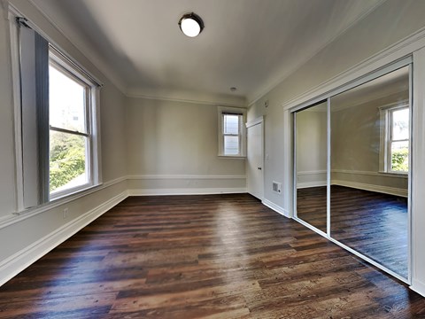 an empty living room with wood flooring and a mirrored door