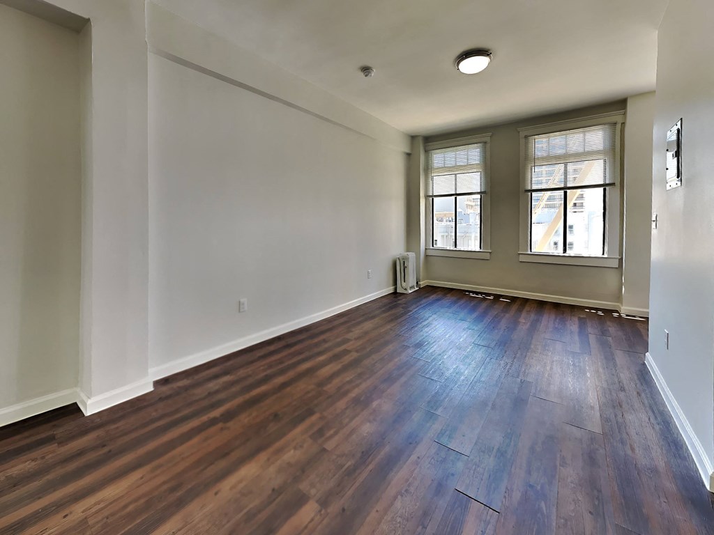 an empty living room with hardwood flooring and two windows