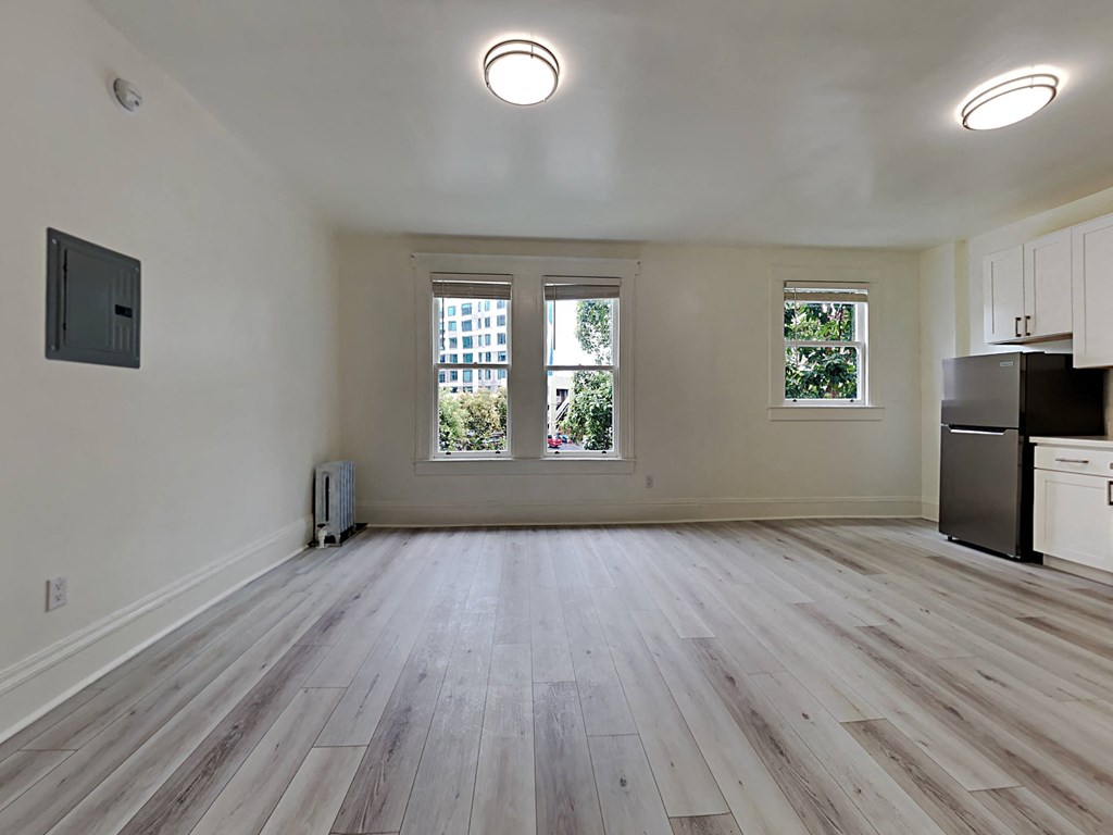 an empty living room with a refrigerator and a window