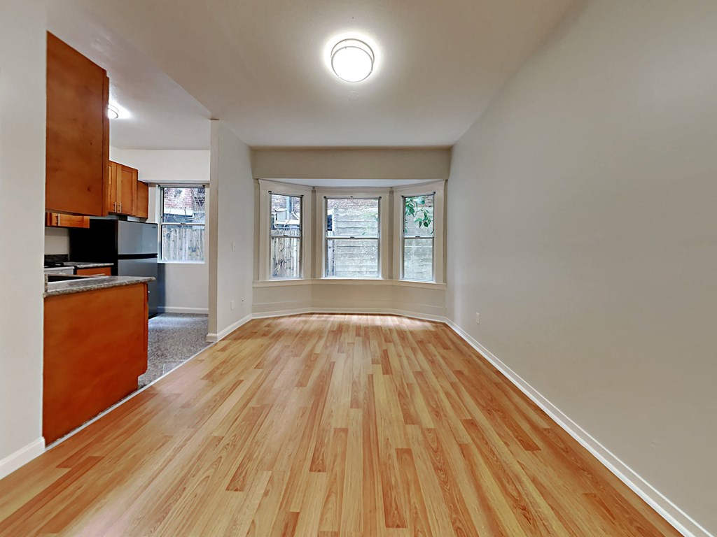 an empty living room with wood floors and a kitchen