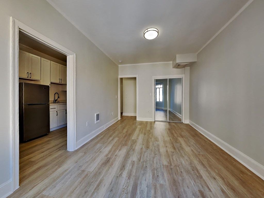 an empty living room with wood flooring and a kitchen