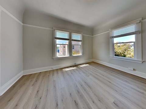 an empty bedroom with wood floors and two windows