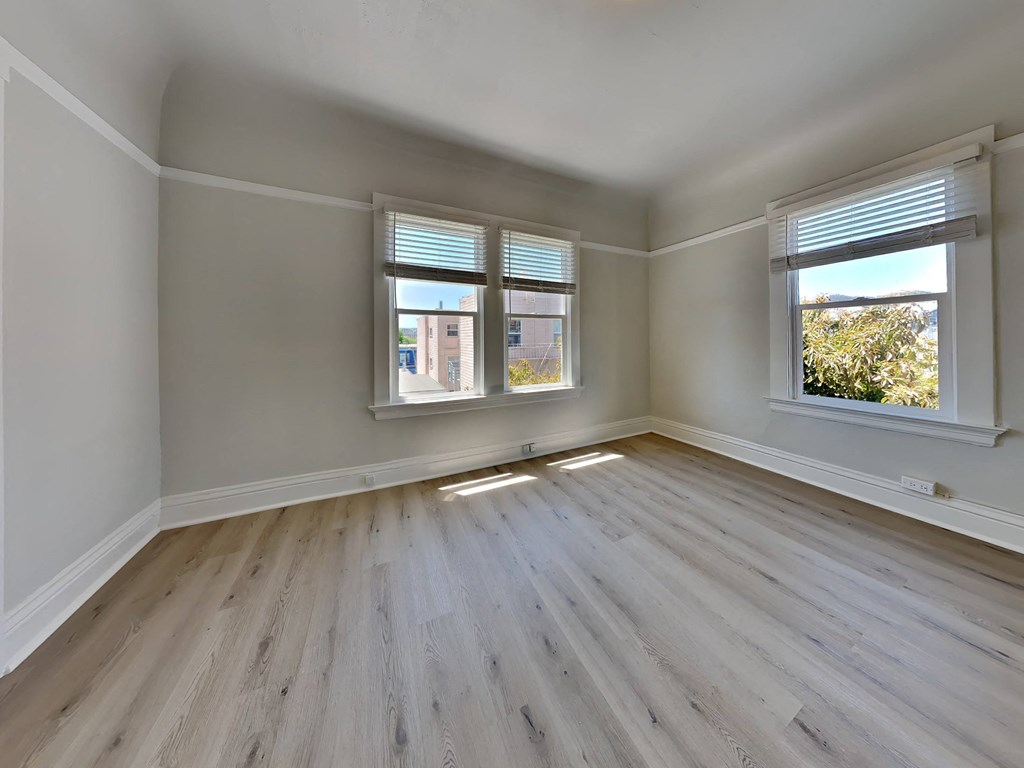 an empty bedroom with wood floors and two windows