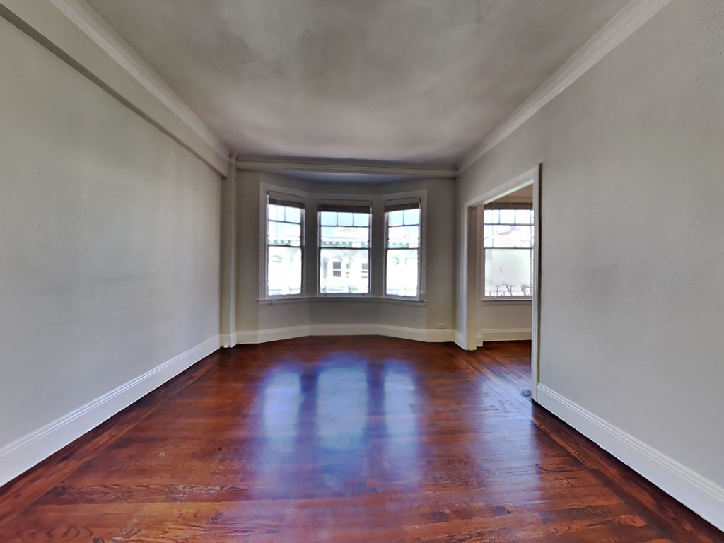 an empty living room with wood floors and three windows