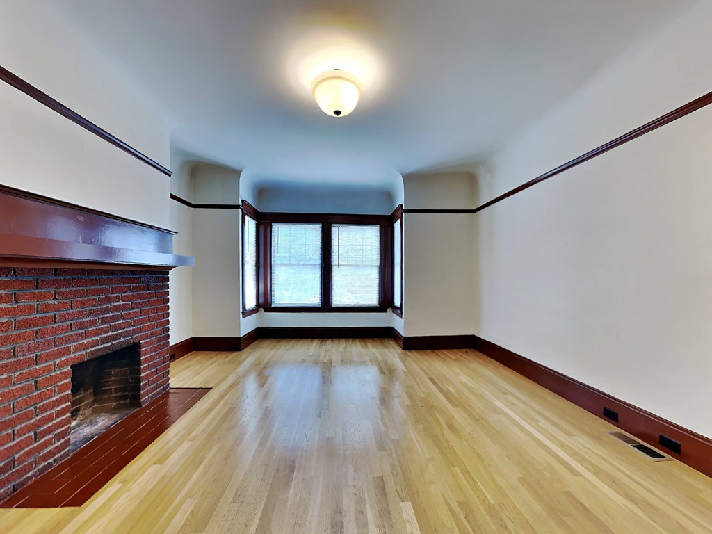 an empty living room with a brick fireplace and wooden floors