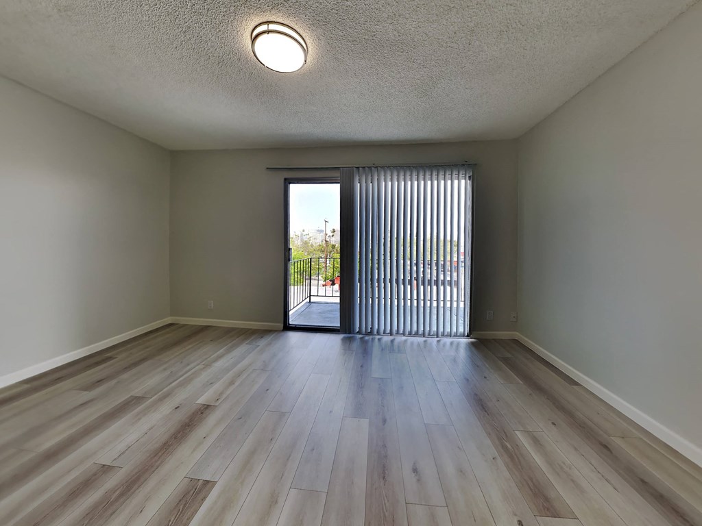an empty living room with wood floors and a door to a balcony