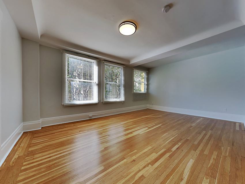 an empty living room with wood floors and three windows