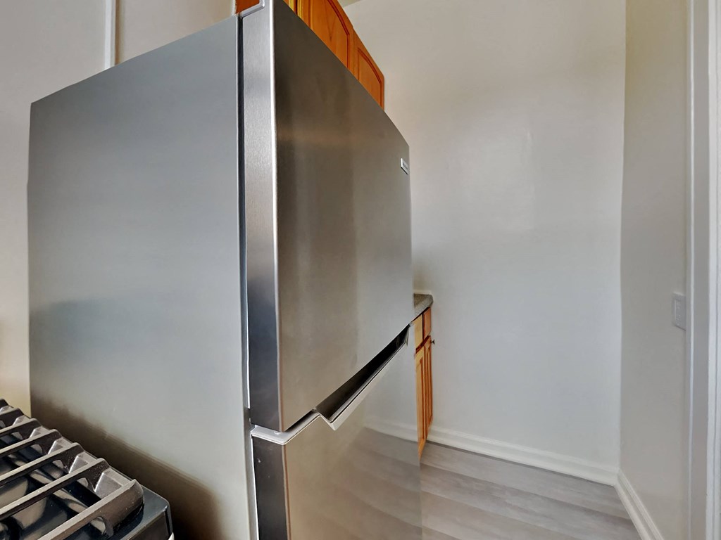 a stainless steel refrigerator in a kitchen with white walls and wood floors