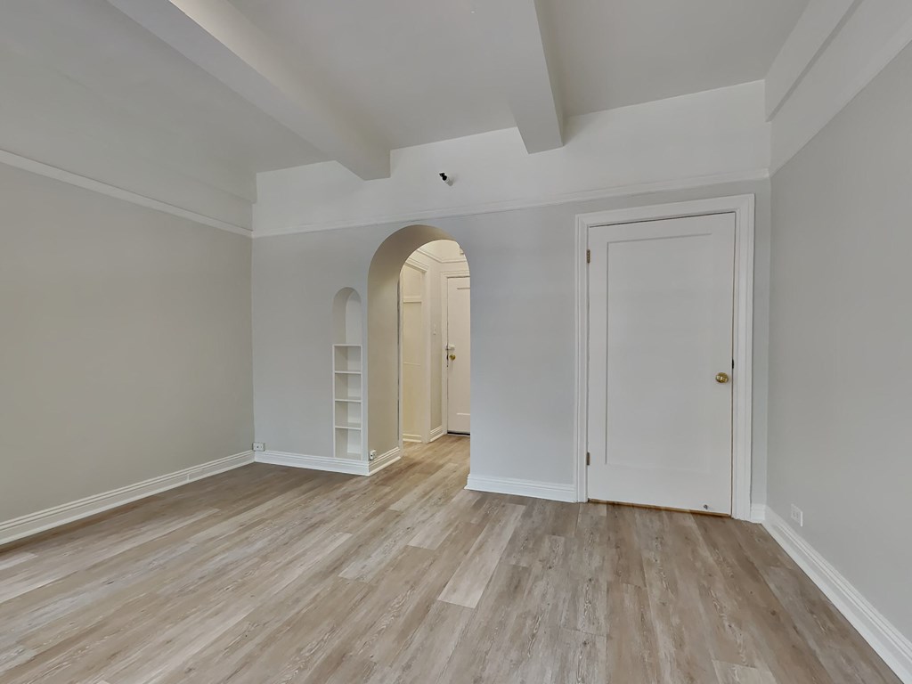 a living room with white walls and wood floors and an arched doorway