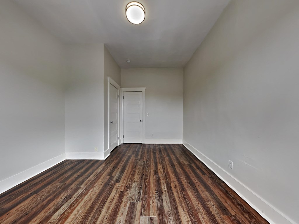 a bedroom with white walls and wood flooring and a door