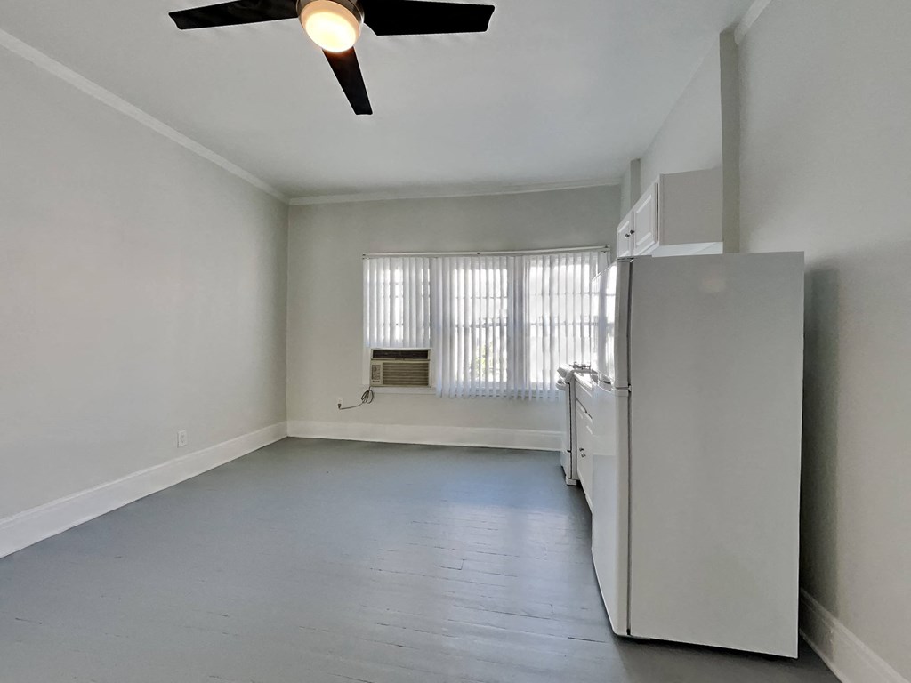 an empty living room with a refrigerator and a window