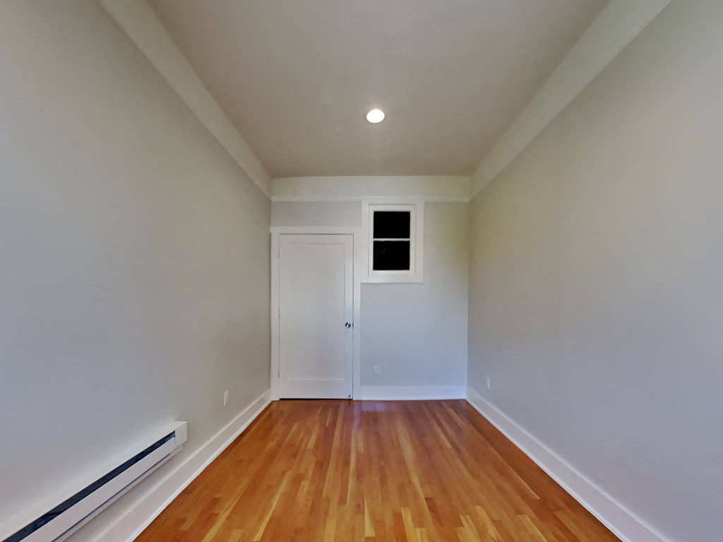 a bedroom with white walls and wood flooring and a window