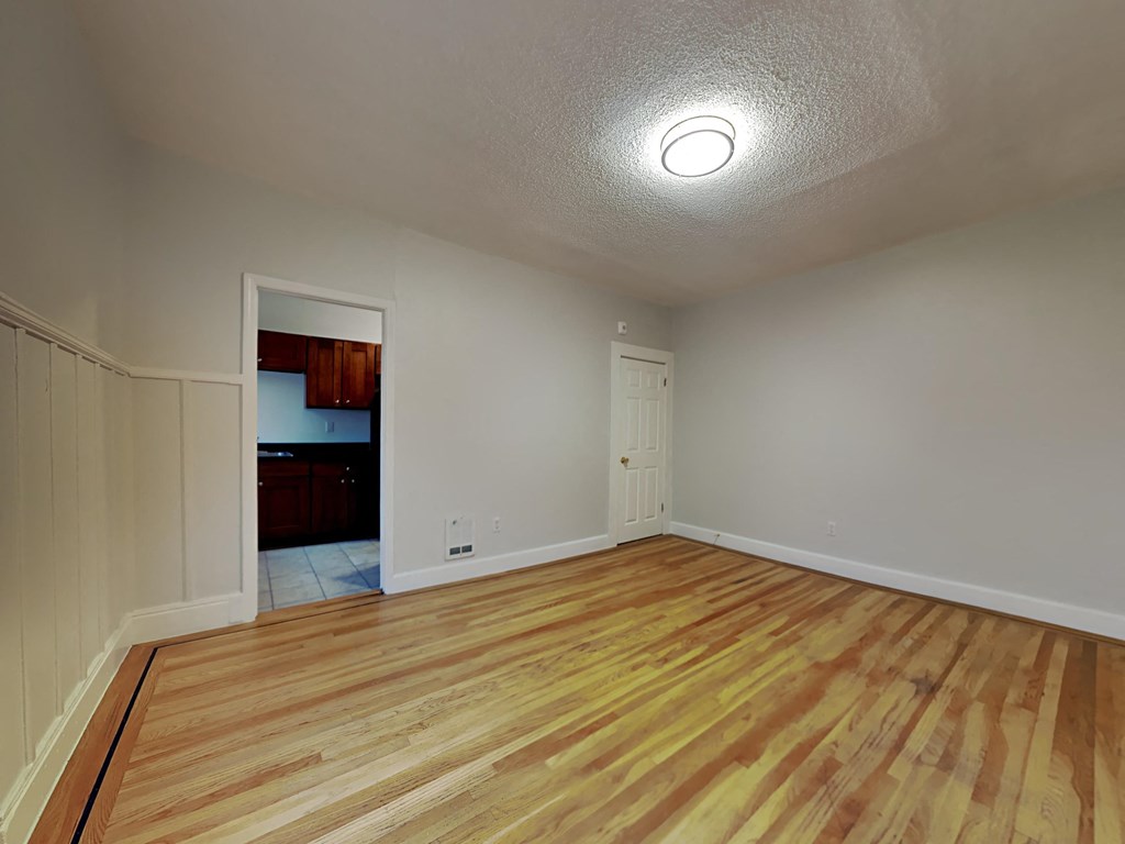 an empty living room with wood flooring and a door to a kitchen