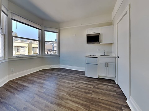 an empty living room with a kitchen and a window