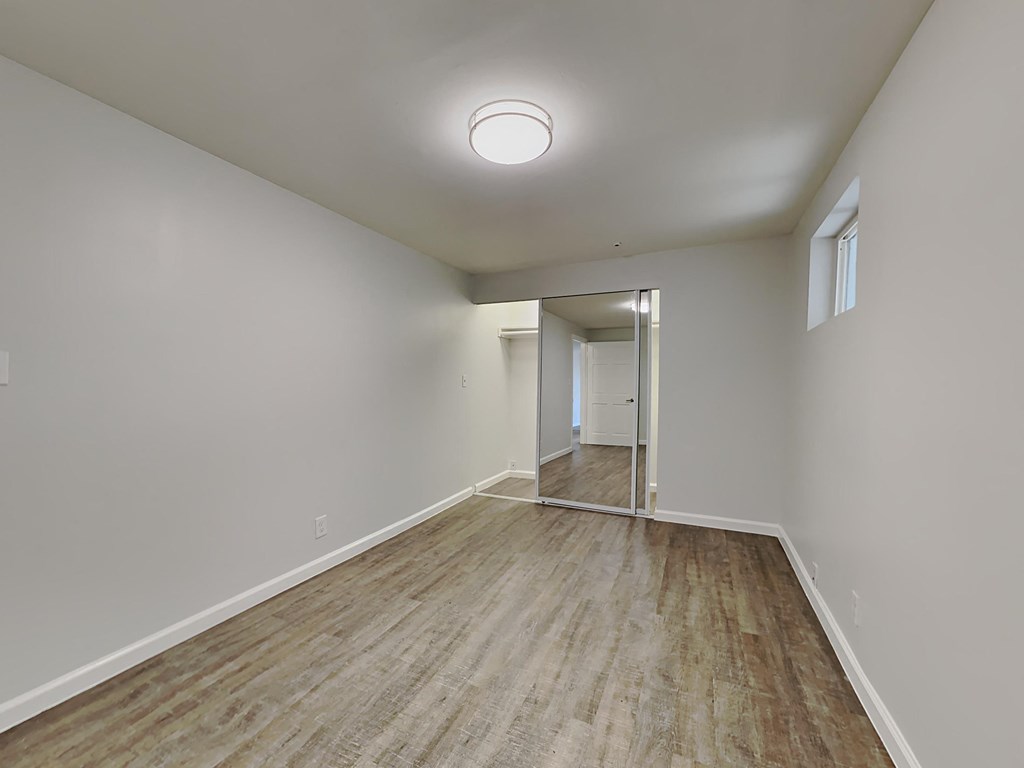 a spacious living room with white walls and wood flooring