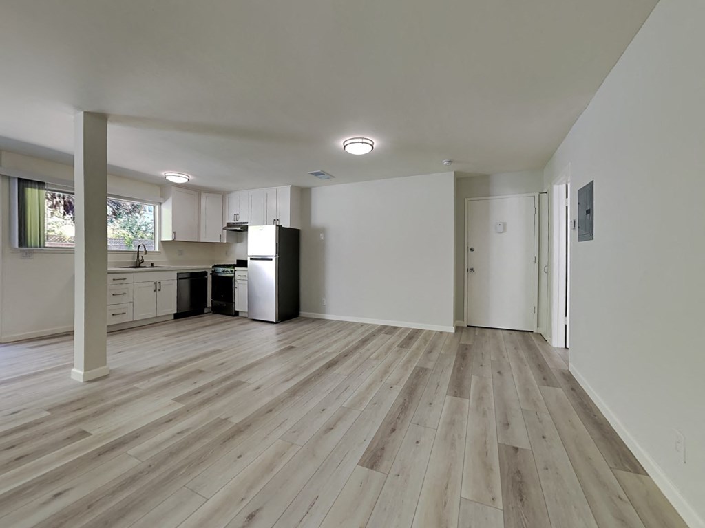 an empty living room and kitchen with wood floors and white walls