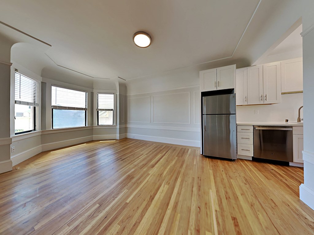 an empty living room with wood floors and a refrigerator