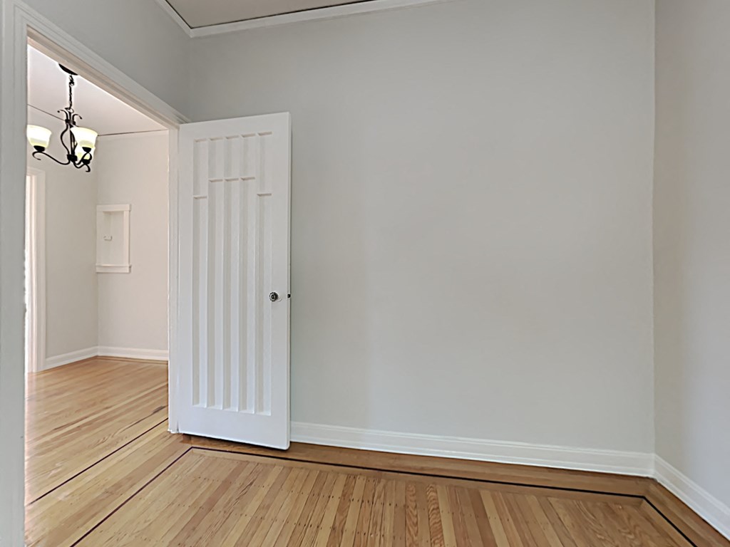 an open door in a room with wood flooring and a white wall and a